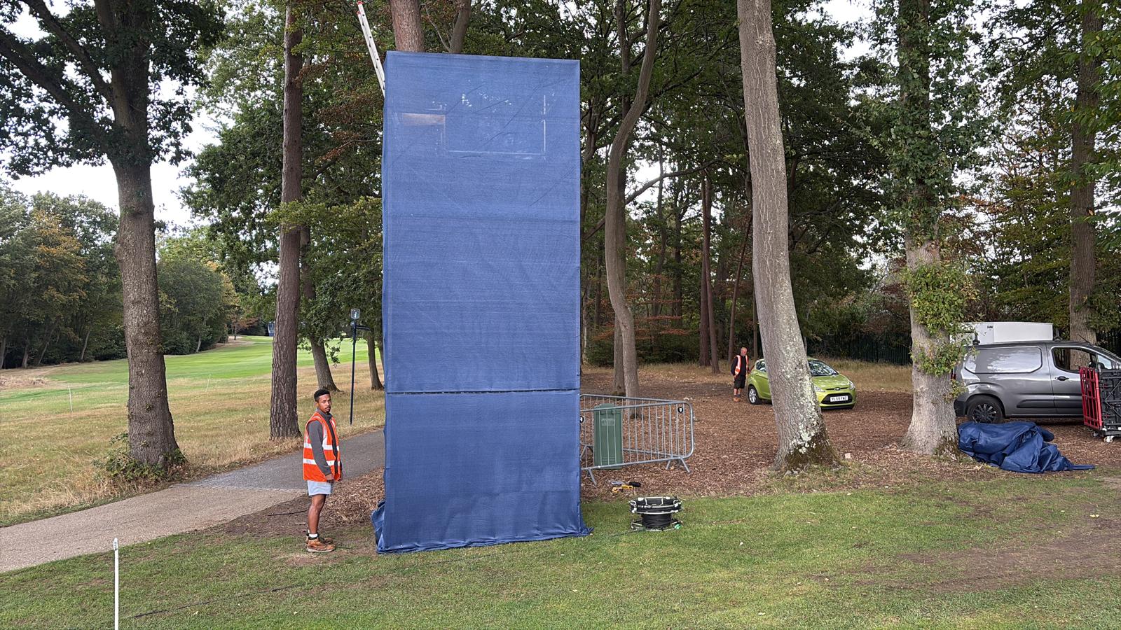 Tall blue-wrapped scaffold camera tower standing on a UK golf course